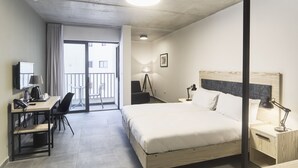 A hotel room with a bed, desk, chair, bedside table, lamp, and a view of the outside balcony. - Mr. Todd Hotel (Sliema)