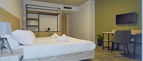 A modern bedroom with a bed, a desk, a chair, a television, and a shelf with towels.