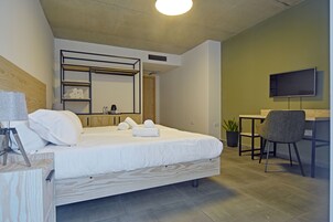 Un dormitorio moderno con una cama, un escritorio, una silla, un televisor y un estante con toallas.
