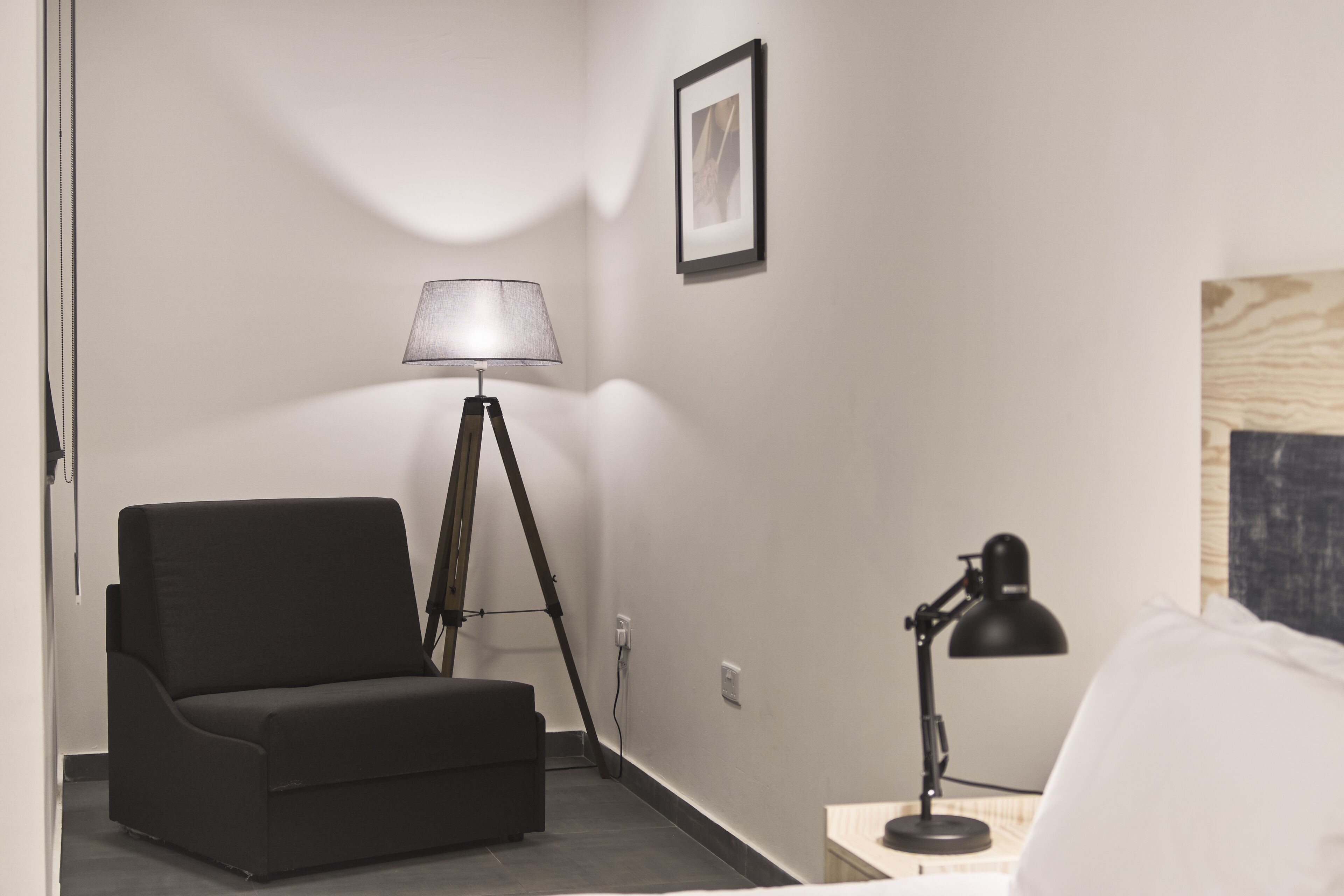 Habitación de hotel con un sofá negro, una lámpara de pie, un escritorio con lámpara y un cuadro enmarcado en la pared.