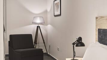 Habitación de hotel con un sofá negro, una lámpara de pie, un escritorio con lámpara y un cuadro enmarcado en la pared.