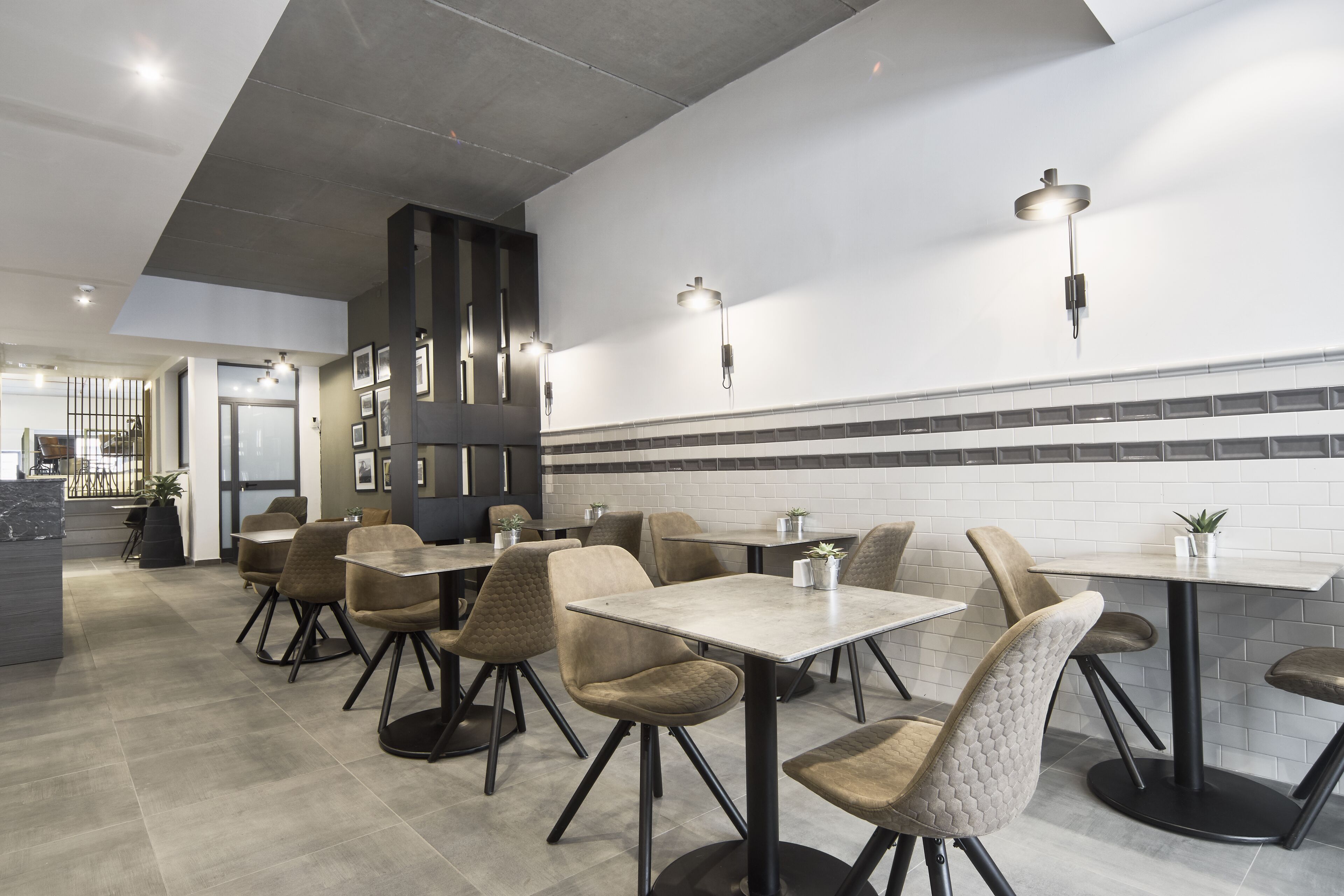 Ein modernes Restaurant-Interieur mit hohen Tischen und Stühlen, eingelassener Beleuchtung und einer gefliesten Rückwand.