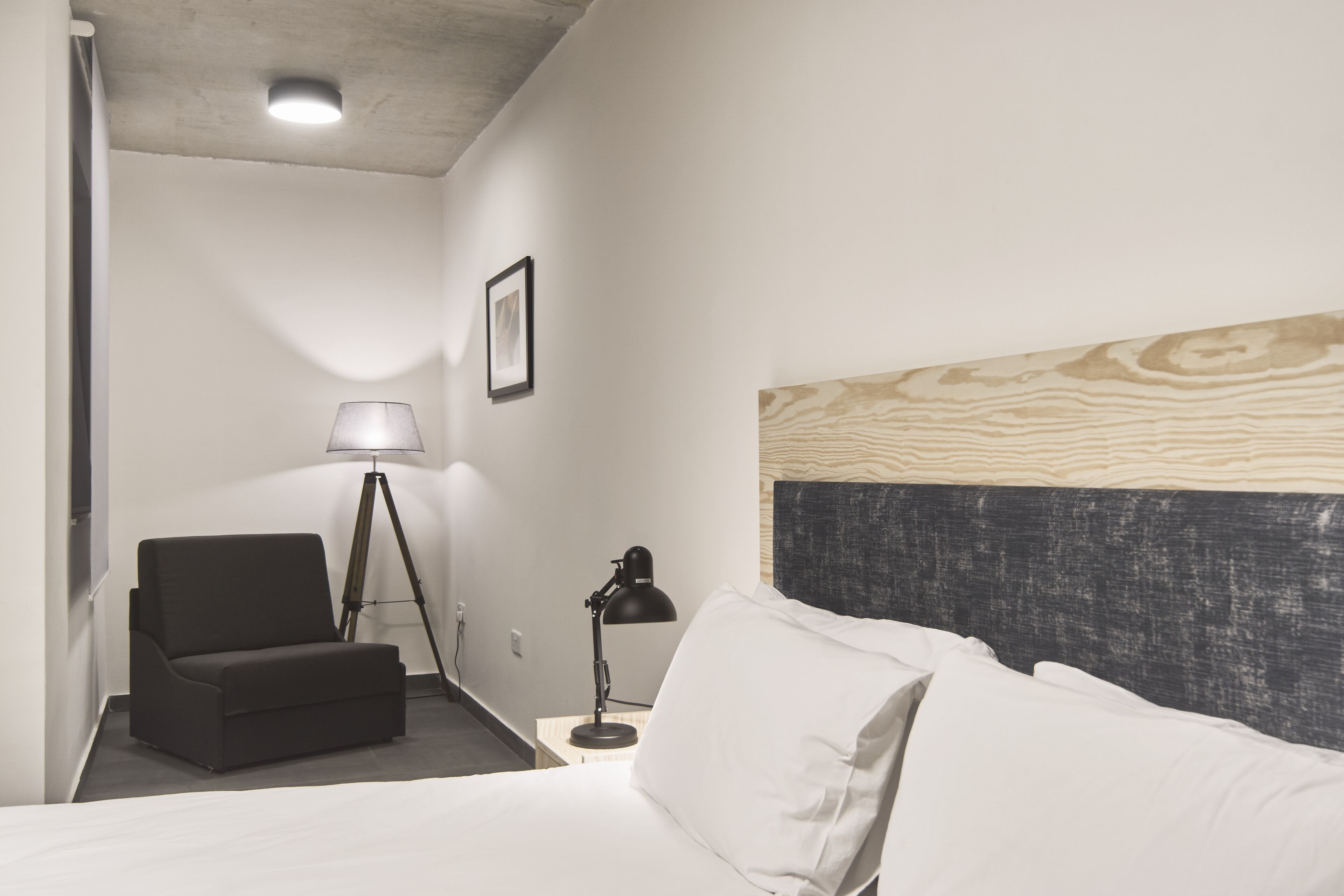 Una habitación de hotel con cama, escritorio, silla, lámpara de pie y un cuadro en la pared.