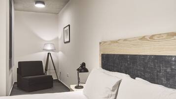 Una habitación de hotel con cama, escritorio, silla, lámpara de pie y un cuadro en la pared.