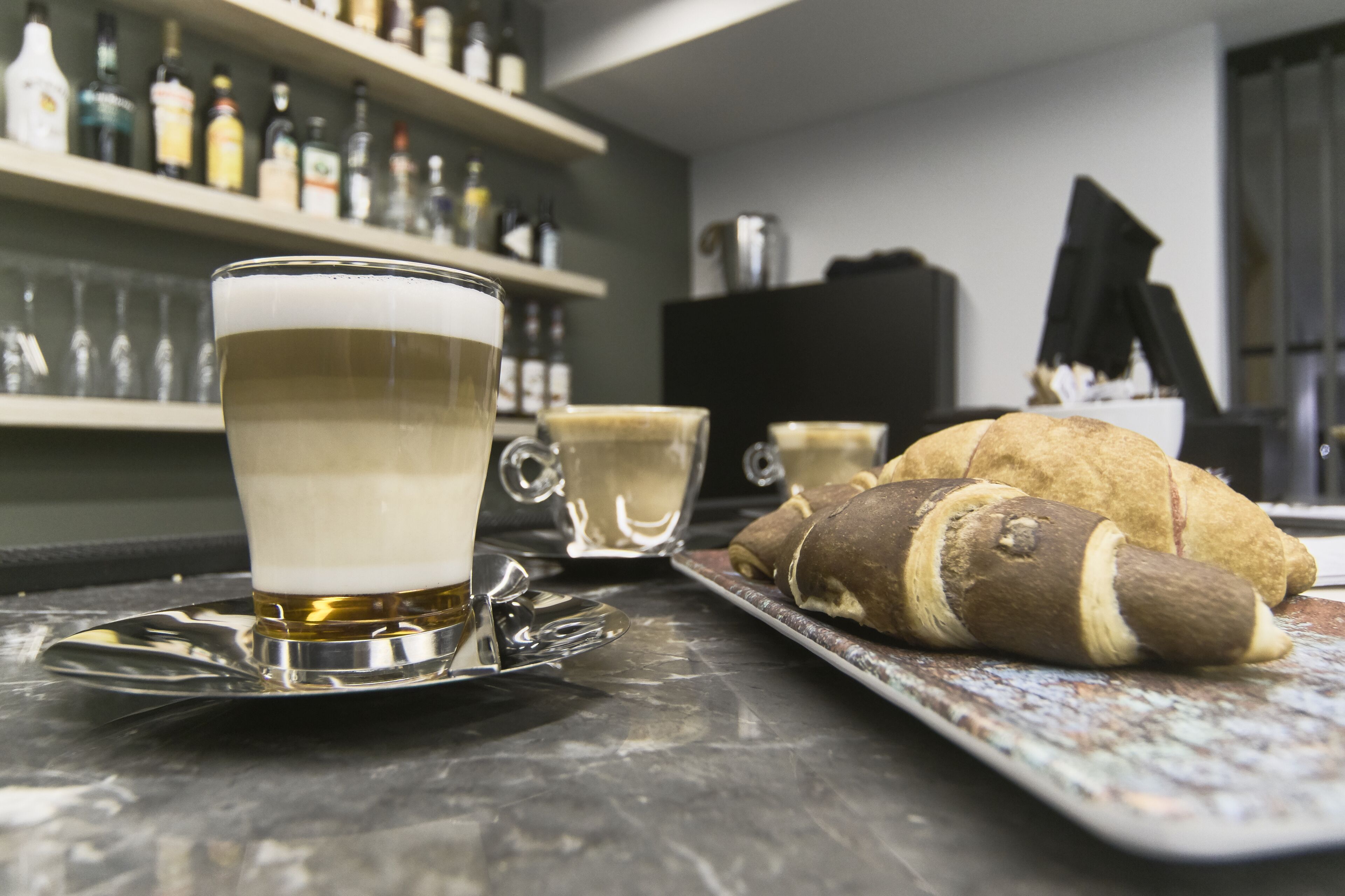 A bar setting with a glass of beer, a croissant, and a tray of pastries on a marble countertop.