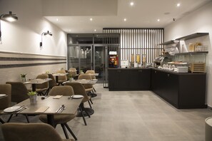 Un espace repas moderne avec des tables et des chaises, un comptoir de cuisine équipé d’appareils électroménagers et un distributeur automatique.