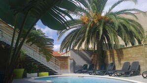 Une piscine avec des chaises longues, un palmier et un escalier menant à un niveau supérieur.