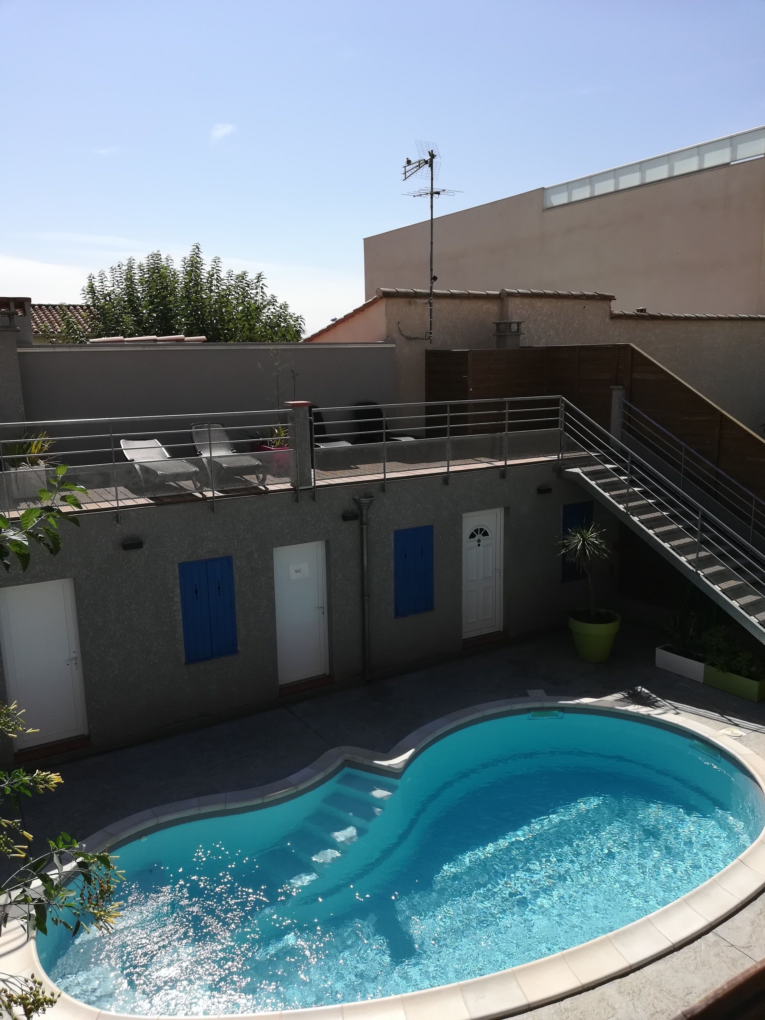 A swimming pool with a sunken center, a covered seating area with chairs, a staircase, and a door marked "WC".