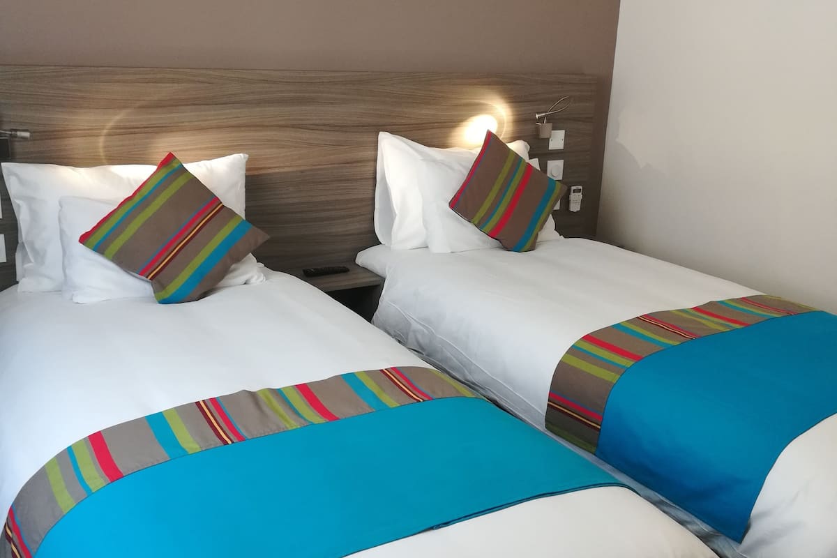 A hotel room with two beds, each with white bedding and colorful striped blankets.