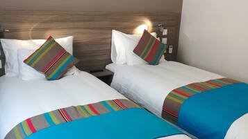 Habitación de hotel con dos camas, cada una con ropa de cama blanca y mantas multicolores a rayas.