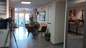 Un hall d'hôtel moderne avec un espace repas, une grande fenêtre donnant sur un château et un panneau indiquant « CHAMBRES ».