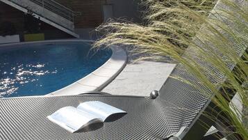 A poolside lounge chair with a book, a pool, and a staircase in the background.
