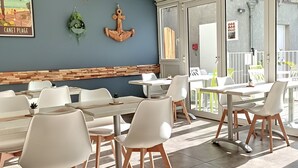 Un restaurant avec des tables et des chaises blanches, un mur décoratif en bois et une vue sur l’espace extérieur aménagé pour les clients.