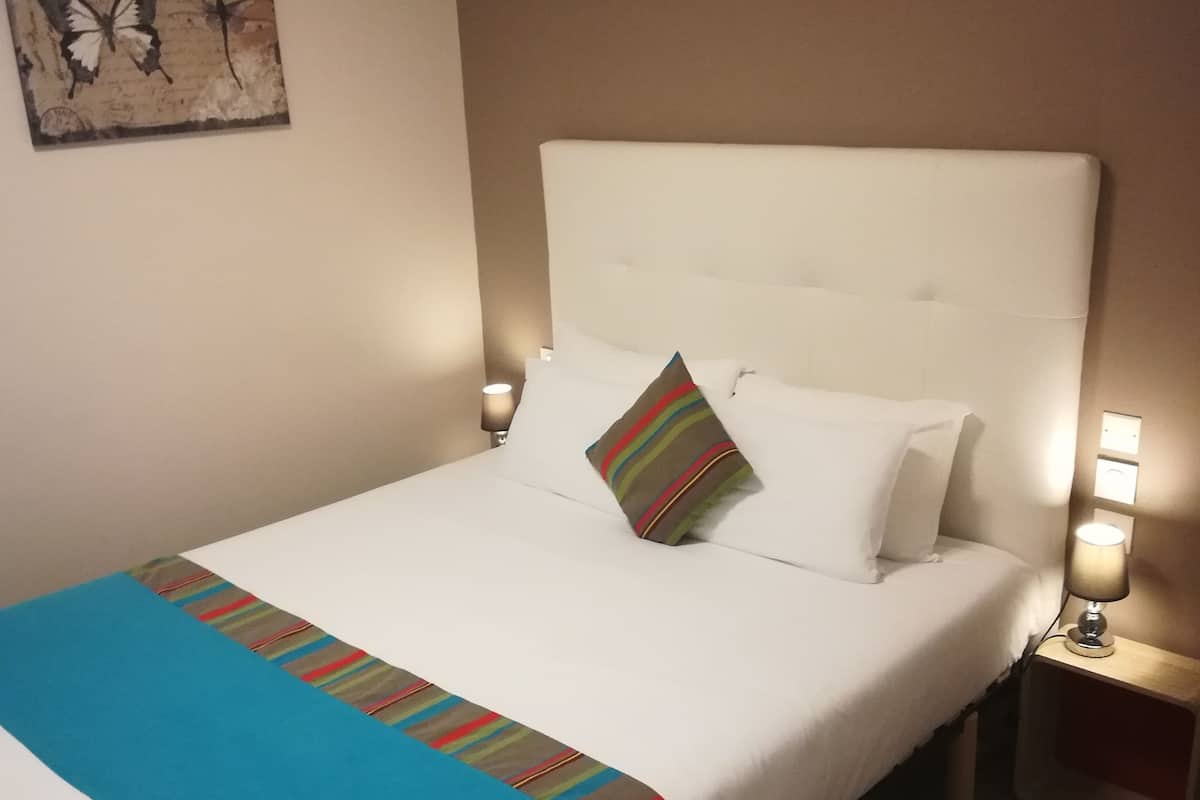 A neatly made bed with a white headboard, a colorful striped blanket, and a single pillow with stripes. There are two bedside lamps on either side of the bed.