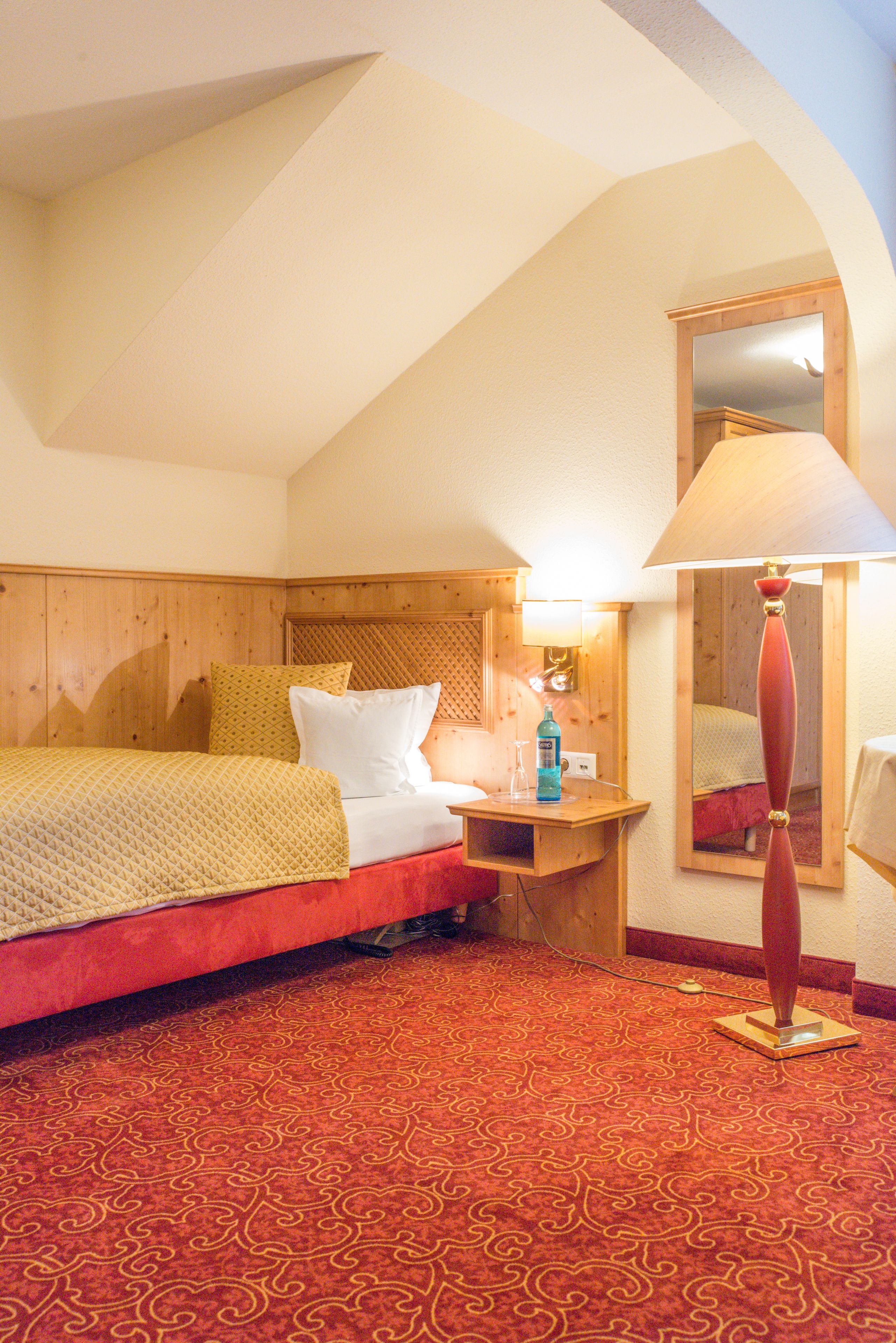 A hotel room with a bed, a nightstand, a lamp, and a mirror.