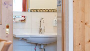 Un baño con lavamanos blanco, espejo y paredes con azulejos.