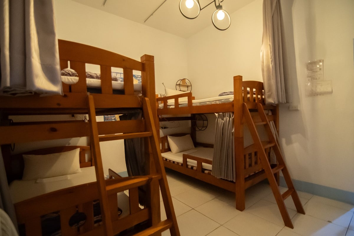 A room with bunk beds, a ladder, a small table, and a ceiling light fixture.