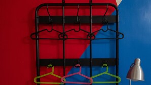 A room with a black metal rack holding colorful hangers, a small table, and a lamp.