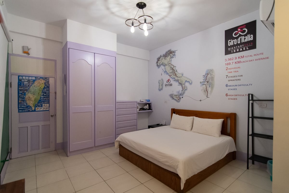 A bedroom with a bed, a wardrobe, a map on the wall, and a ceiling light fixture.