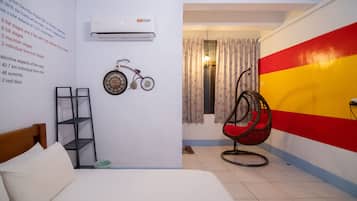 A room with a bed, a wall-mounted air conditioner, a bicycle, a wicker chair, and a colorful wall.