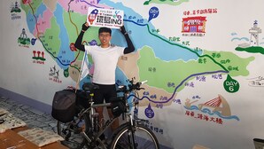 A person standing in front of a wall with a colorful map and a bicycle.