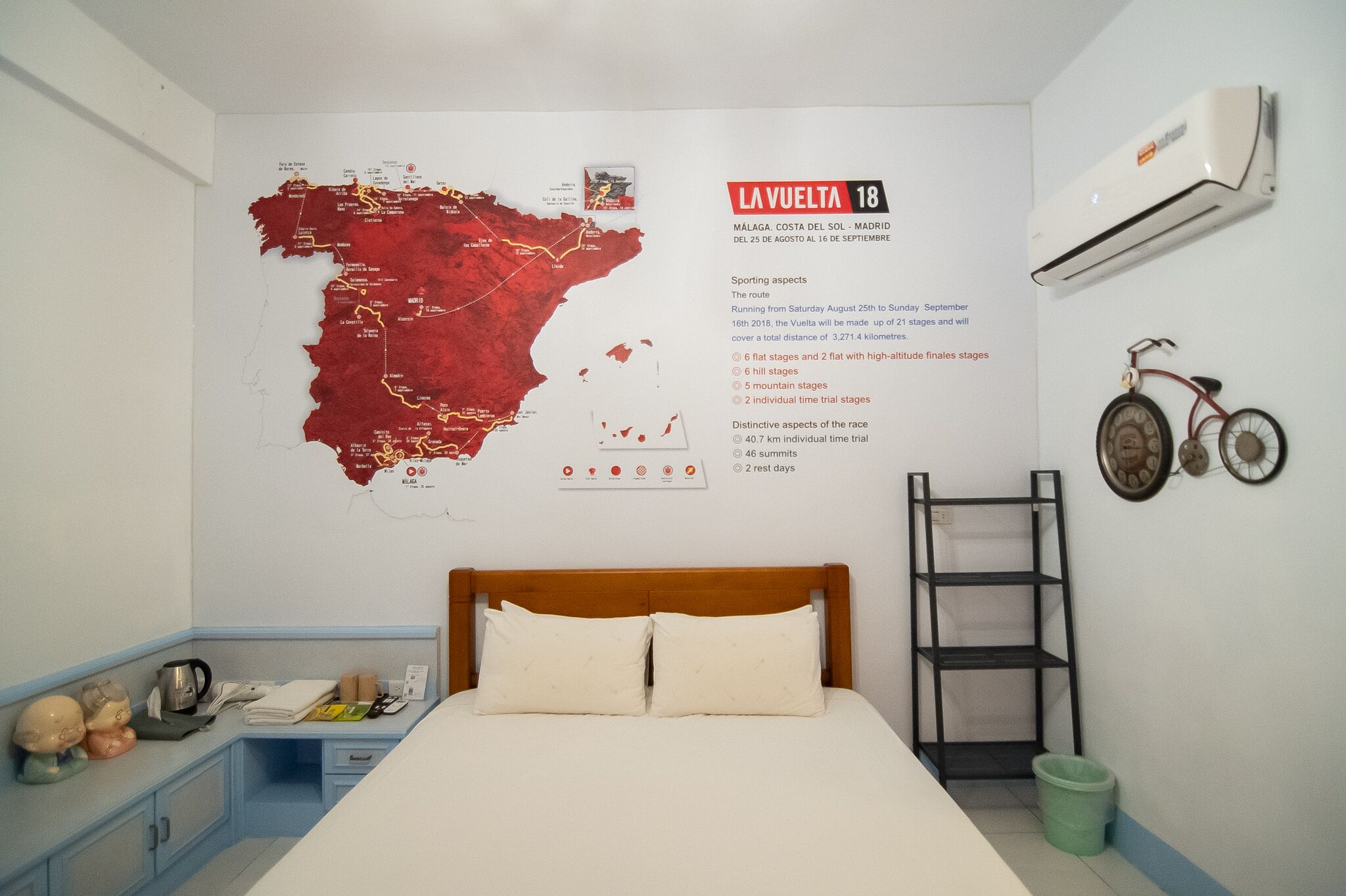 Una habitación de hotel con una cama, un mapa en la pared, una bicicleta y una escalera.