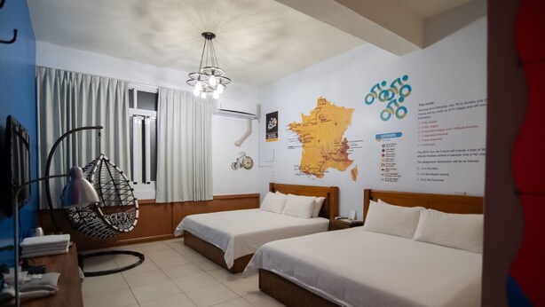 A hotel room with two beds, a hanging chair, a map on the wall, and a window with curtains.