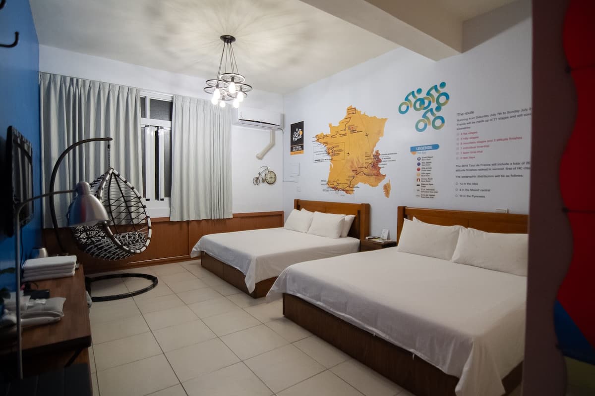 A hotel room with two beds, a hanging chair, a map on the wall, and a window with curtains.