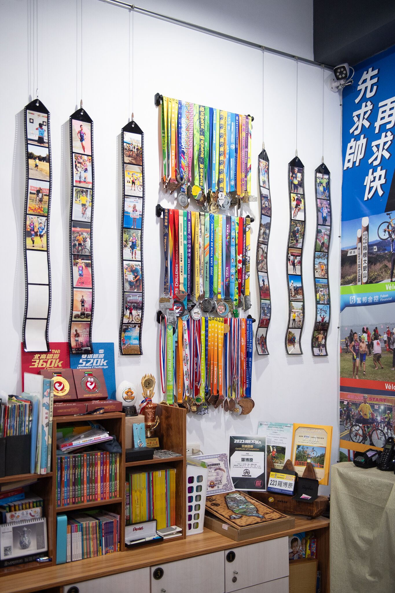 A room with a wall displaying medals and ribbons, a bookshelf with books, and a desk with a computer and papers.