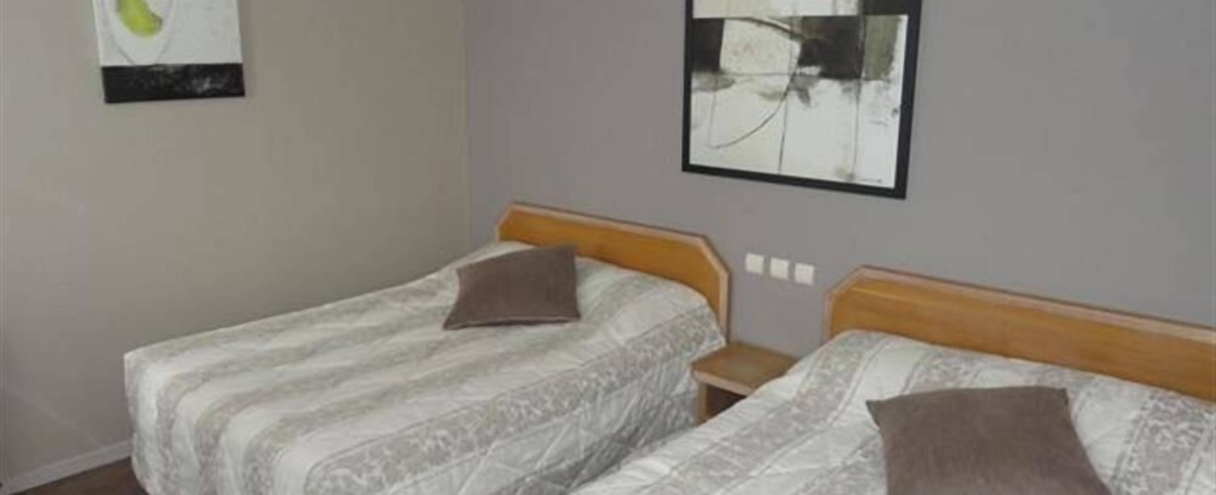 Ein Zimmer mit zwei Einzelbetten, beide mit Holz Kopfteilen und einem gemusterten Bettbezug. An jedem Bett steht ein kleiner Nachttisch.