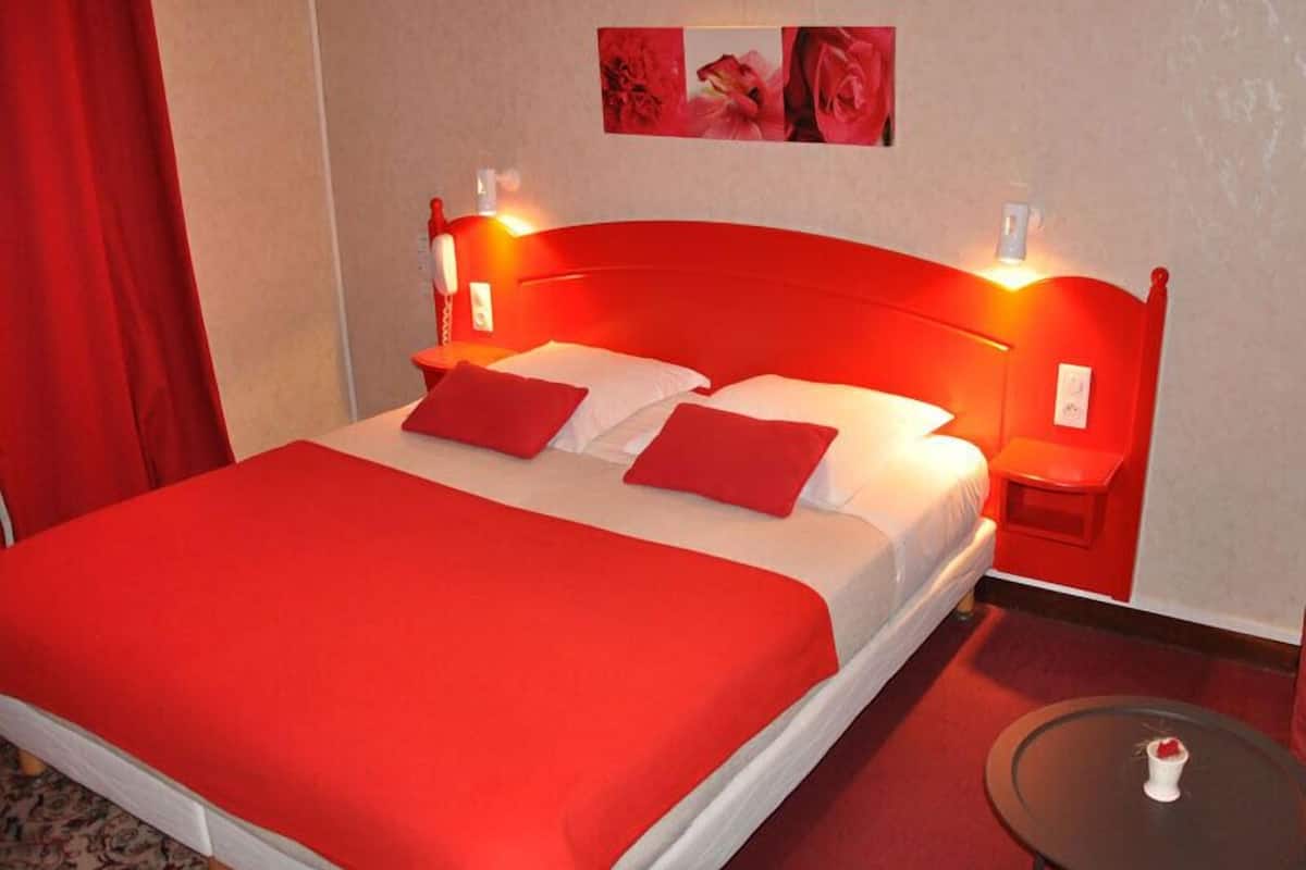 Een hotelkamer met een rode sprei, een passend rood hoofdeinde en rode accenten op de nachtkastjes.
