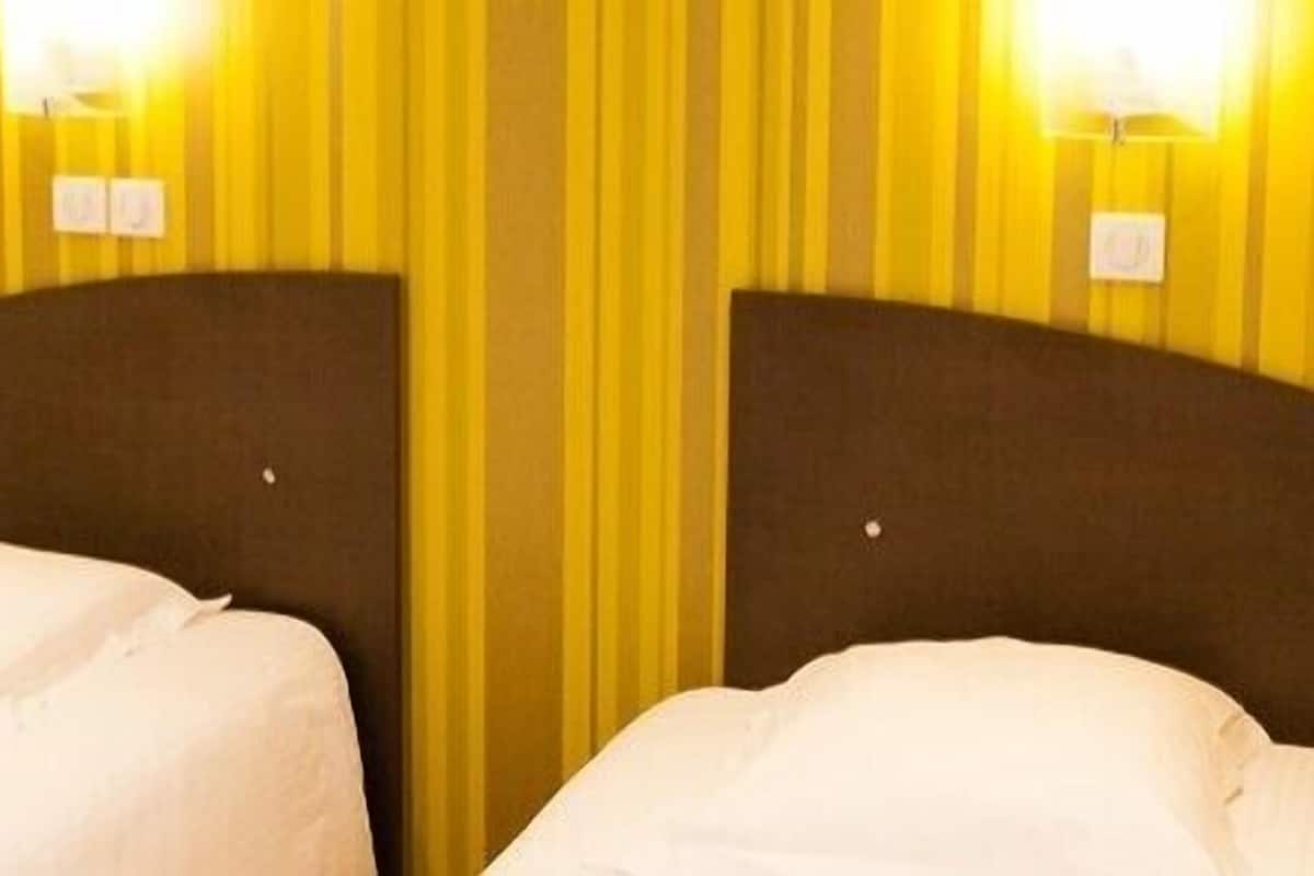 Een hotelkamer met twee enkele bedden, elk met een gebogen hoofdeinde en een witte spreidek.