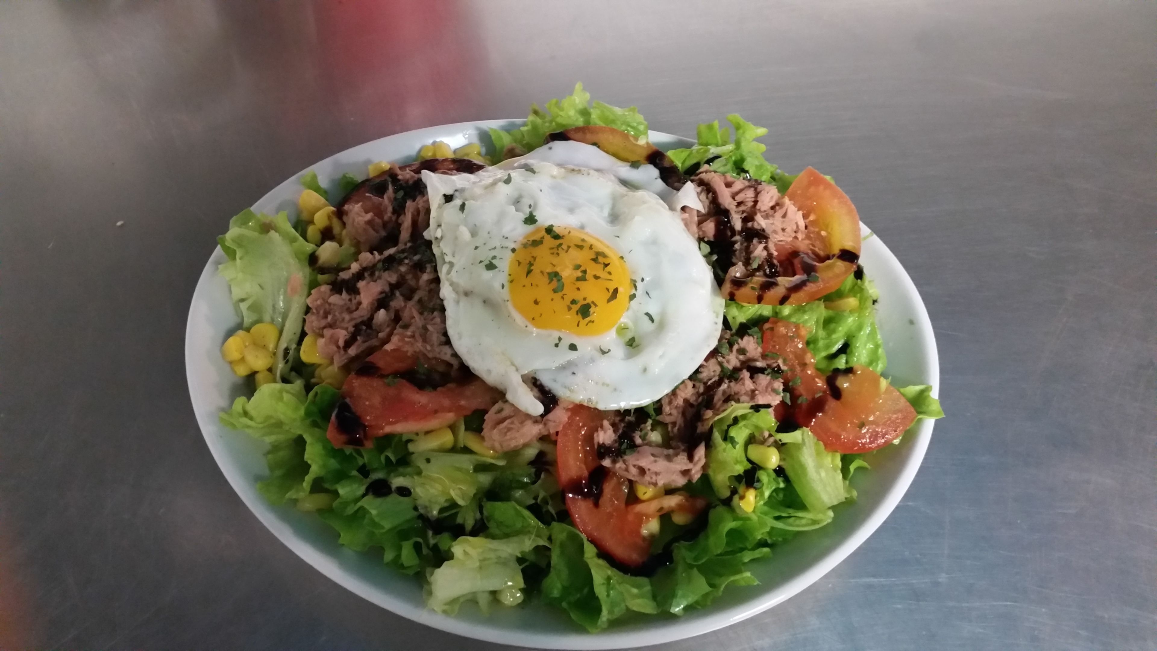 A salad with lettuce, tomatoes, corn, and a fried egg on top.