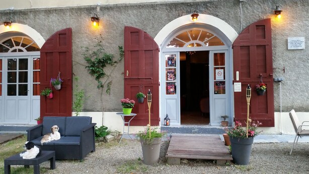 Un bâtiment avec des portes et des fenêtres rouges, des places assises à l’extérieur et des plantes en pot.