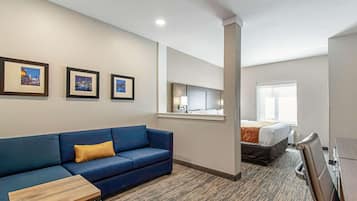 Ein Hotelzimmer mit einem blauen Sofa, einem kleinen Holztisch, einem Bett mit weißer und orangefarbener Bettdecke, einem Fenster und gerahmten Bildern an der Wand.