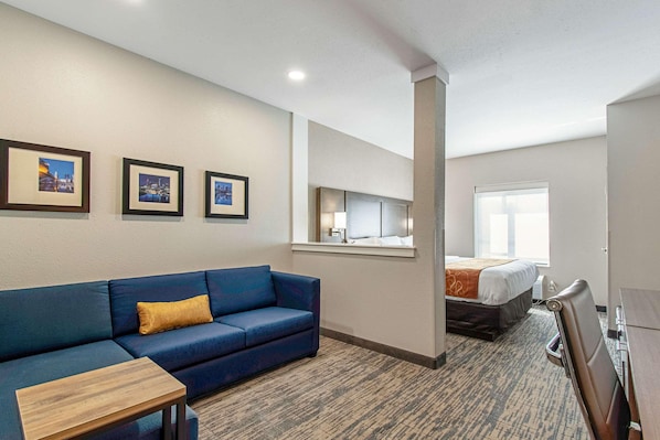 Une chambre d’hôtel avec un canapé bleu, une petite table en bois, un lit recouvert d’une courtepointe blanche et orange, une fenêtre et des tableaux encadrés accrochés au mur.