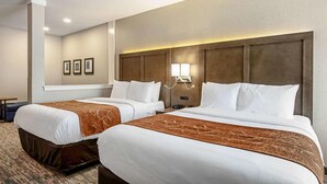 Ein Hotelzimmer mit zwei Betten, einem Kopfteil mit integrierter Beleuchtung sowie einem kleinen Tisch und einem Stuhl.