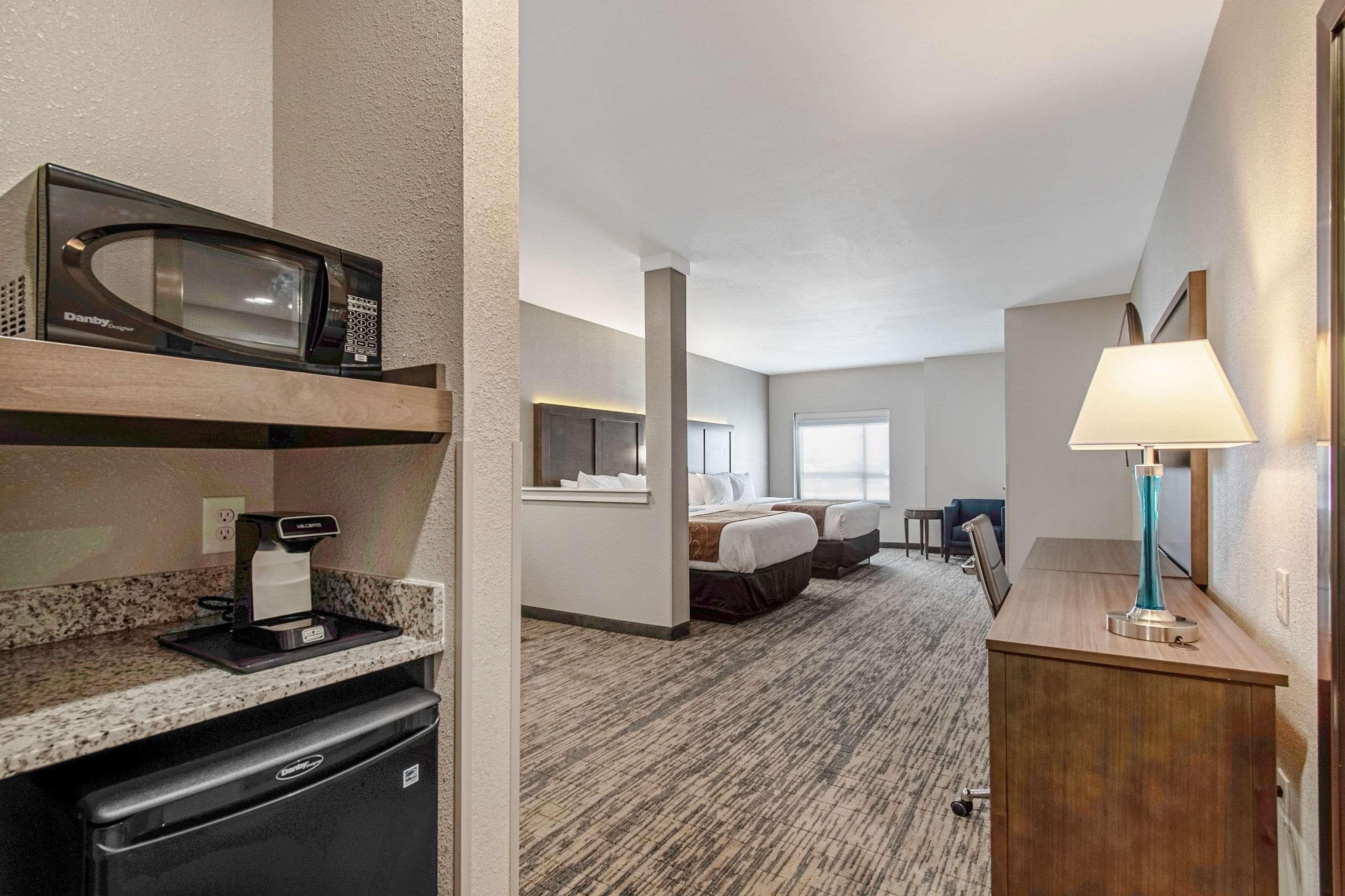 A hotel room with a kitchenette, a bed, a desk, and a lamp.