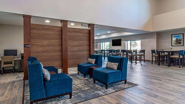 Een ruime lobby met blauwe fauteuils, een houten scheidingswand en een eetgedeelte met tafels en stoelen.