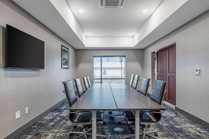 Un salón de conferencias con una larga mesa, sillas, un televisor de pantalla plana y un amplio ventanal.