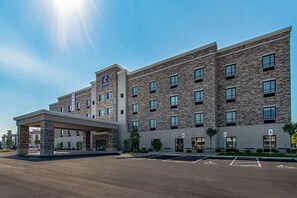 Un hotel de varios pisos con fachada de piedra, un acceso cubierto y un estacionamiento con espacios para discapacitados.