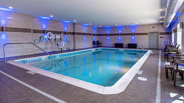 Ein Hallenbad mit klarem Wasser, umgeben von Liegestühlen und einem Rettungsschwimmerstuhl.