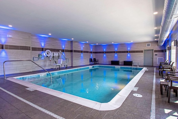 Une piscine intérieure à l’eau claire, entourée de chaises longues et d’une chaise de maître-nageur.