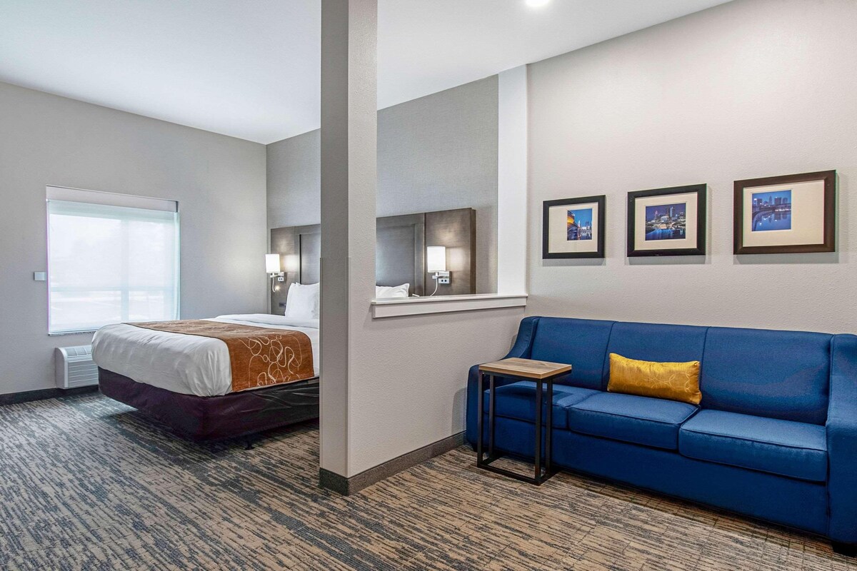Een hotelkamer met een bed, een blauwe bank, een kleine tafel en drie foto's in lijsten aan de muur.