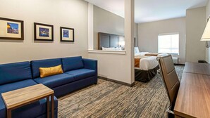 Een hotelkamer met een blauwe bank, een houten tafel, een bed met hoofdeinde, een raam en wanddecoratie.