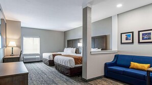 Een hotelkamer met twee bedden, een blauwe bank, een bureau en een raam.