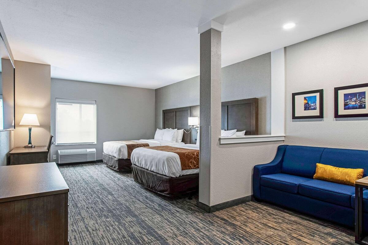 Une chambre d’hôtel avec deux lits, un canapé bleu, un bureau et une fenêtre.