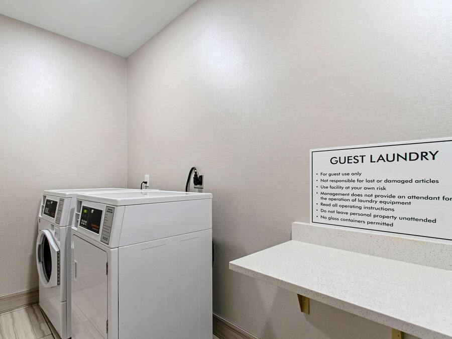 Zona de lavandería para huéspedes con lavadora y secadora, un cartel con instrucciones de uso y una pequeña encimera.