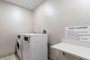 Un espace buanderie à la disposition des clients, comprenant un lave-linge et un sèche-linge, un panneau indiquant les instructions d’utilisation et un petit comptoir.