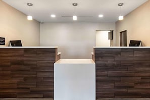 Un espace d’accueil au design moderne, avec un comptoir central blanc encadré de panneaux en bois, un éclairage suspendu et une porte visible au fond.